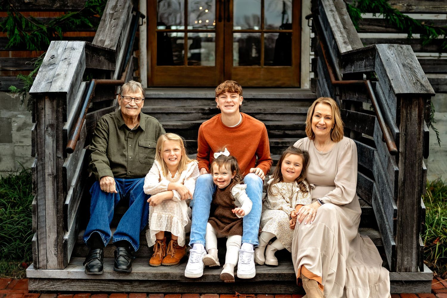A family sits together on rustic wooden steps outside a building wearing coordinated casual fall outfits.
