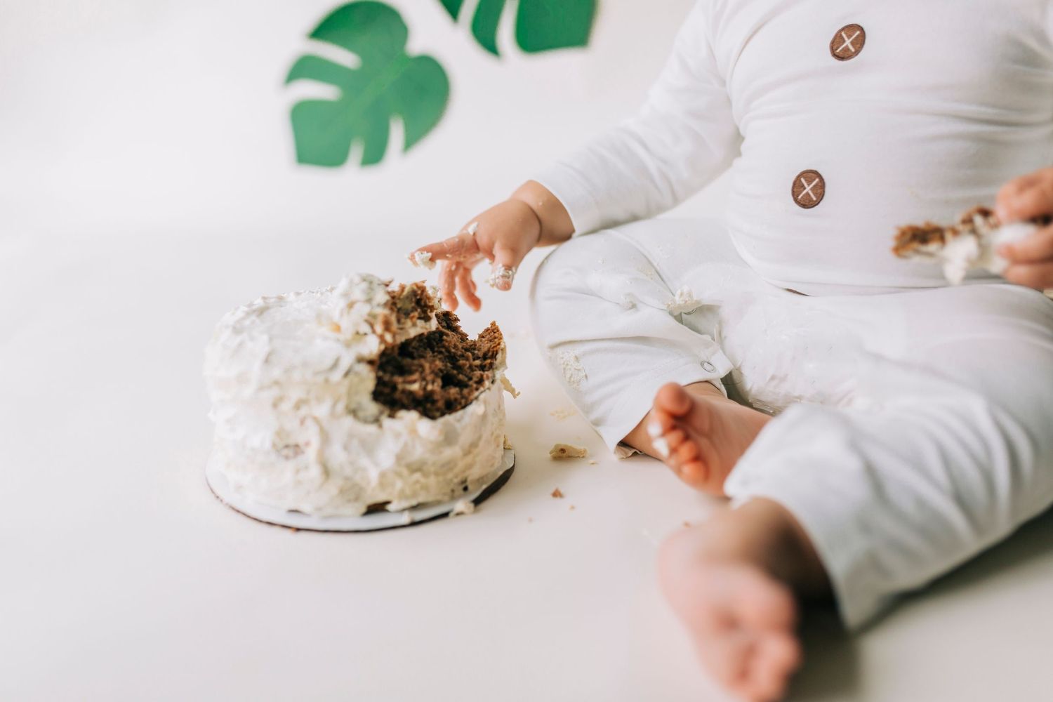 Someone in a white sweater reaching for a smashed and destroyed white frosted cake on a light surface.