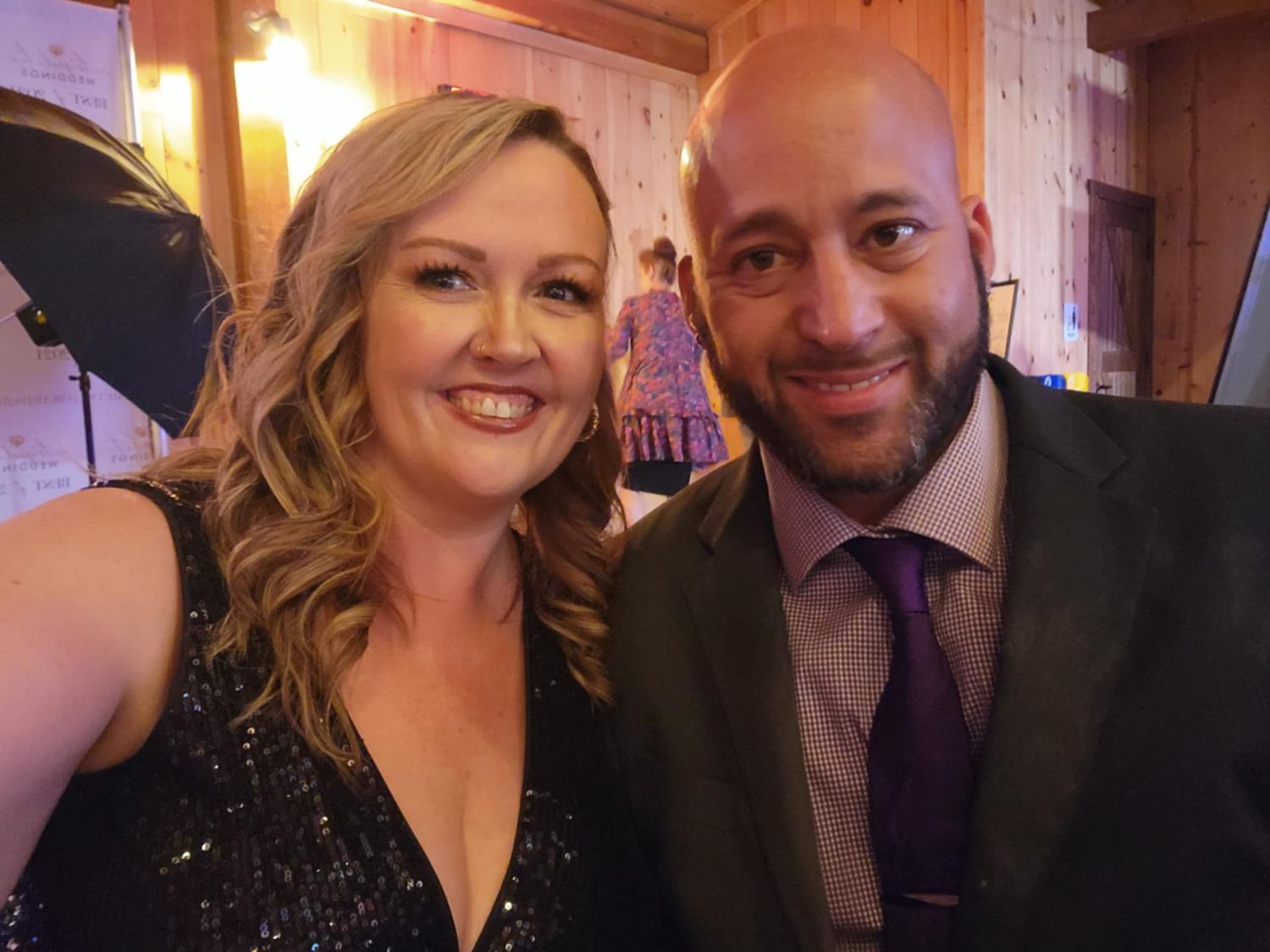 A couple posing together at a formal event, with the woman wearing a sparkling black dress and the man in a suit and tie.
