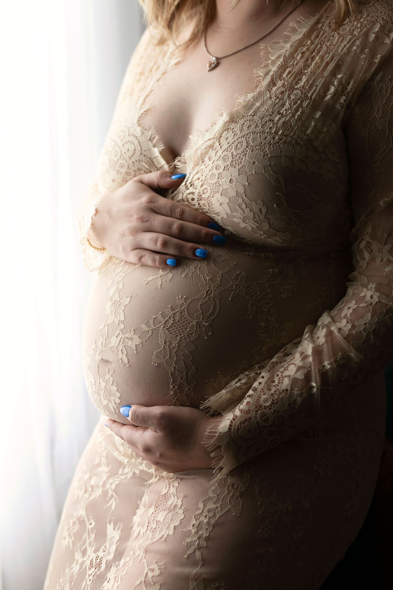 Close-up shot of a pregnant woman's belly in lace maternity wear with hands gently resting on the bump.