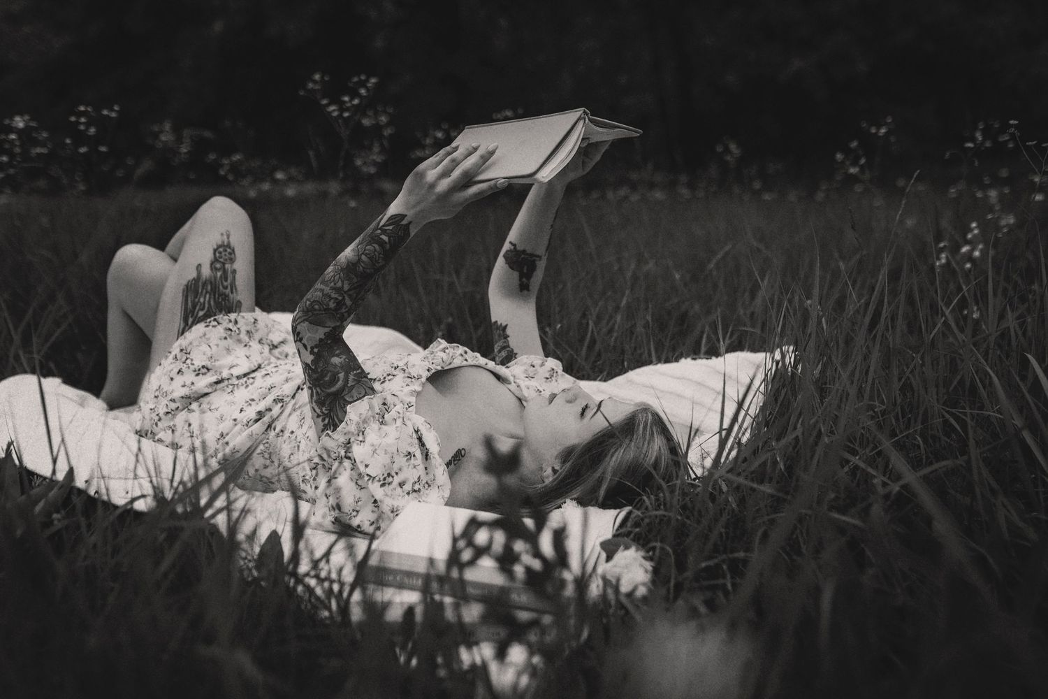 Person lying in tall grass while reading a book outdoors in black and white photography.