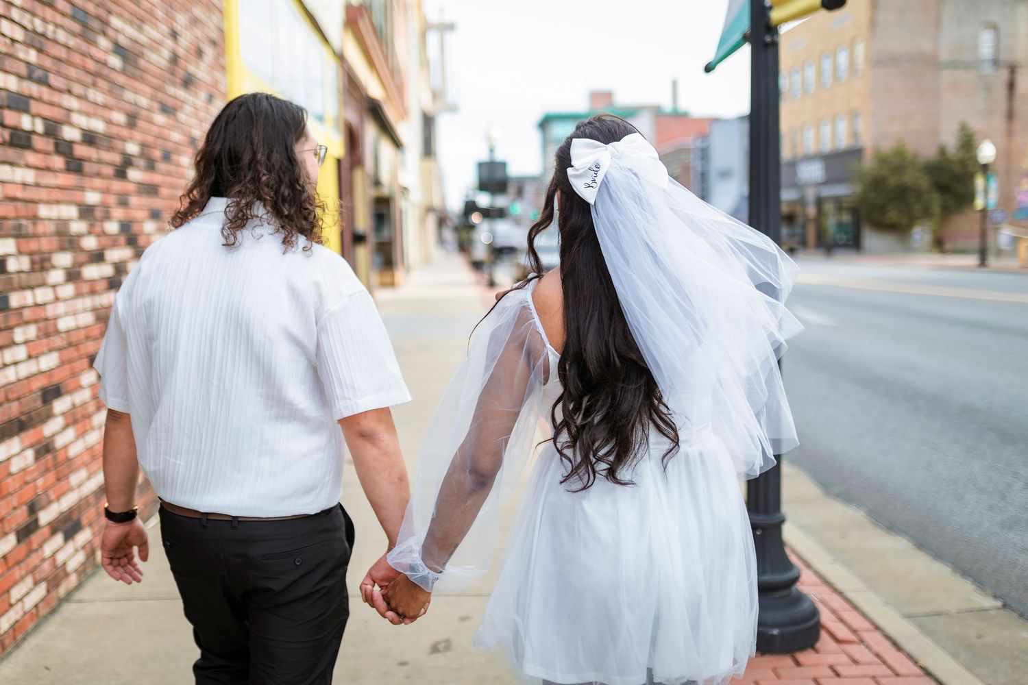 Couple in black and white attire walking hand in hand down a brick-lined urban street during their wedding celebration.