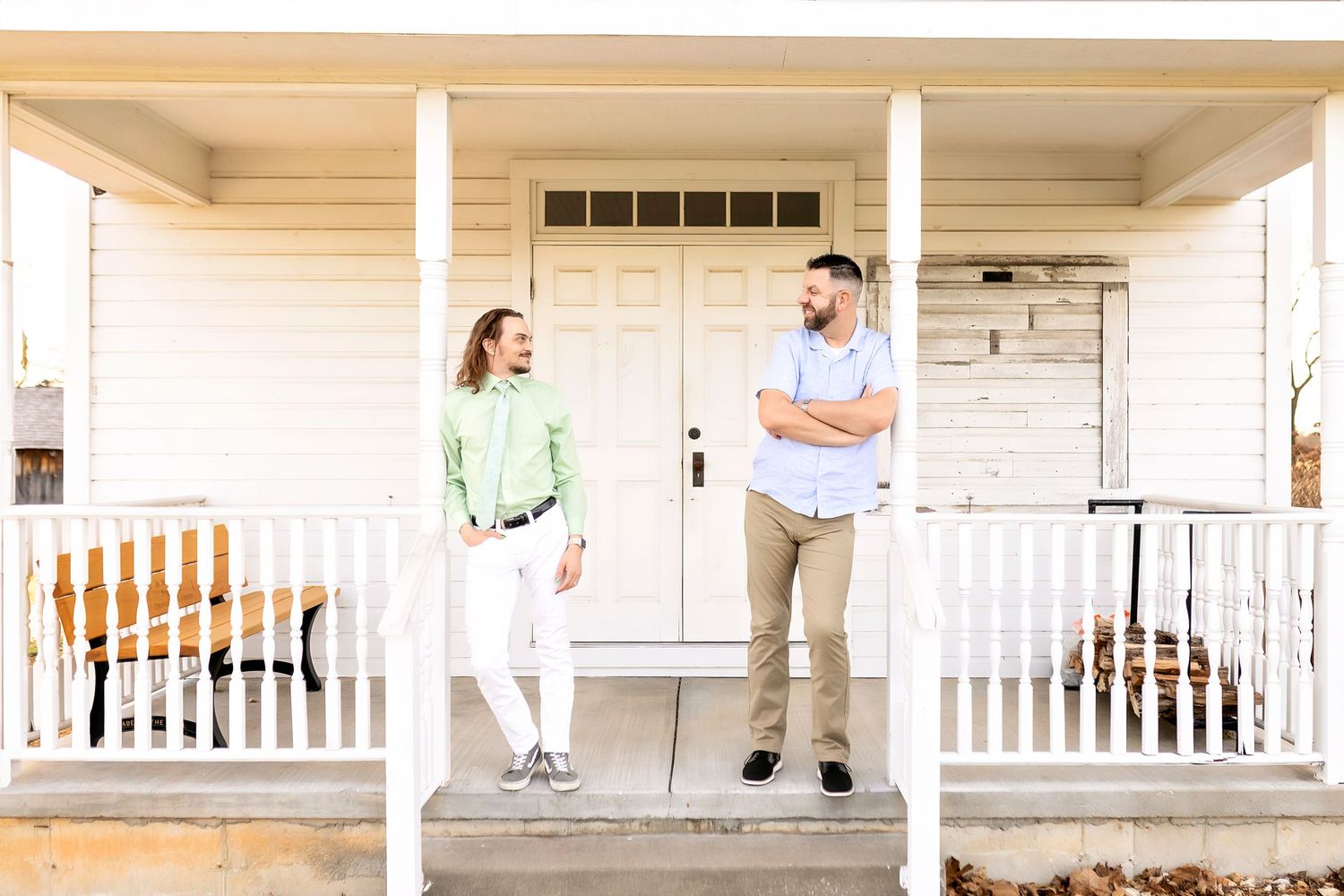 Two men standing on a white porch with columns having a conversation at the entrance of a traditional home.