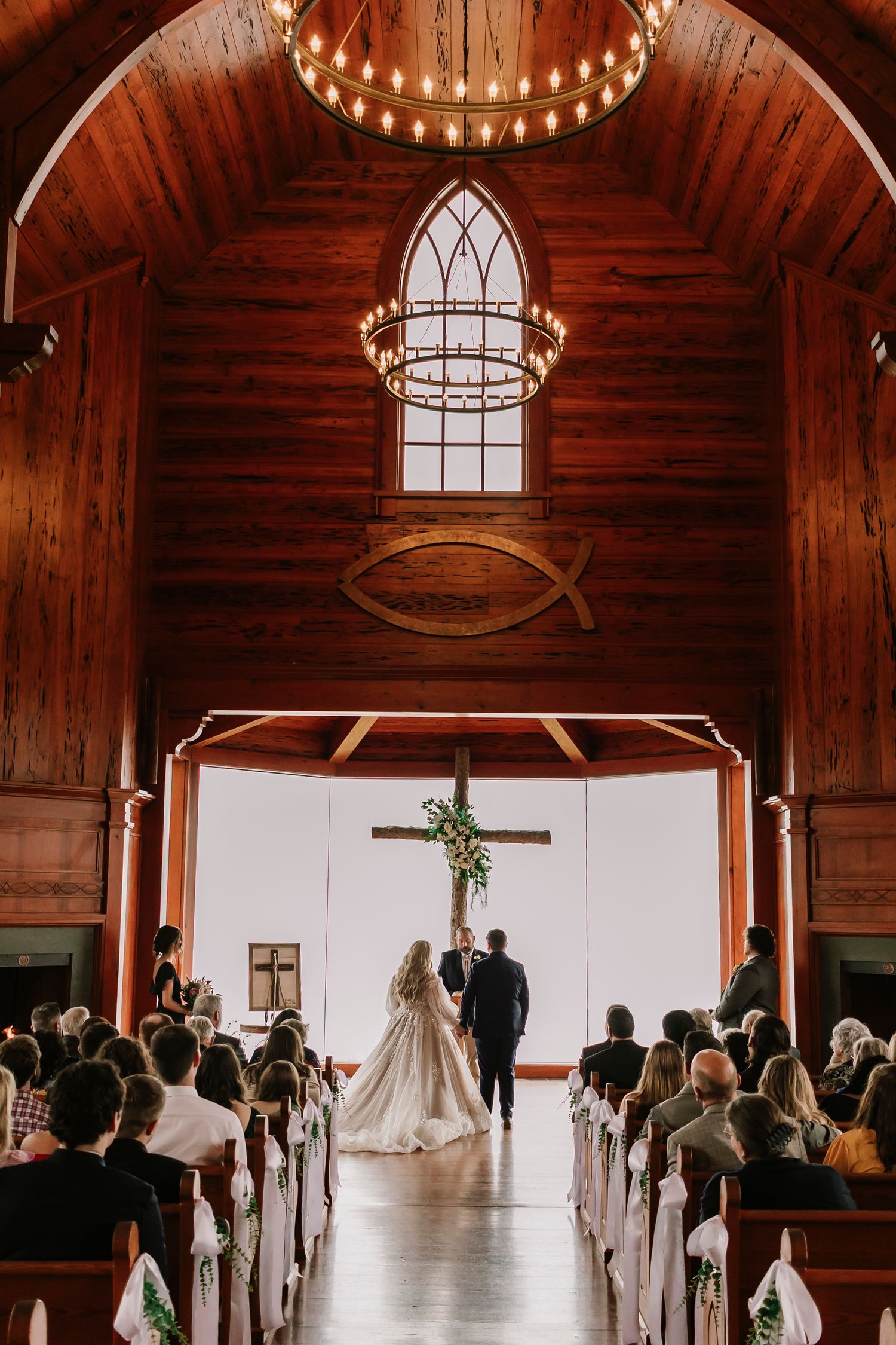 Wedding ceremony in a rustic wooden chapel with cathedral windows, chandeliers and Christian cross at the altar at Top of the Rock Chapel.