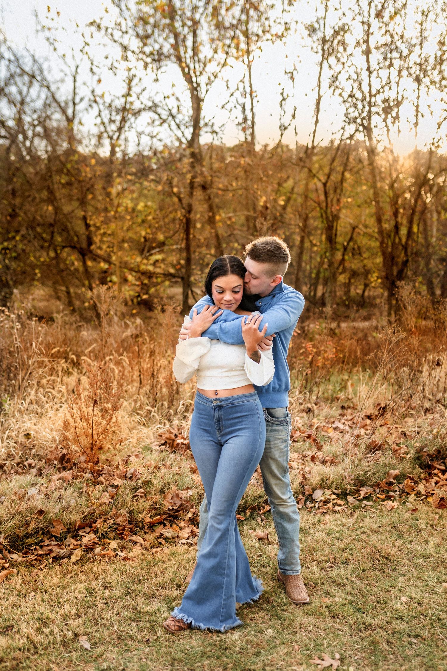 Romantic autumn outdoor photoshoot of couple embracing in casual denim outfits against golden fall foliage.