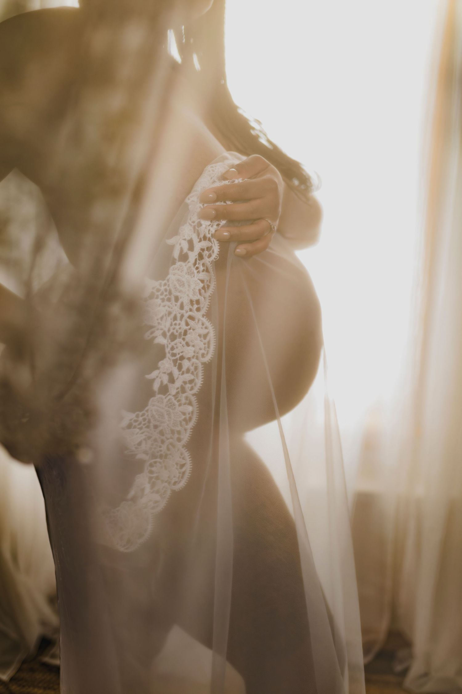 A wedding dress with delicate lace details is illuminated in soft, dreamy backlight while being photographed.