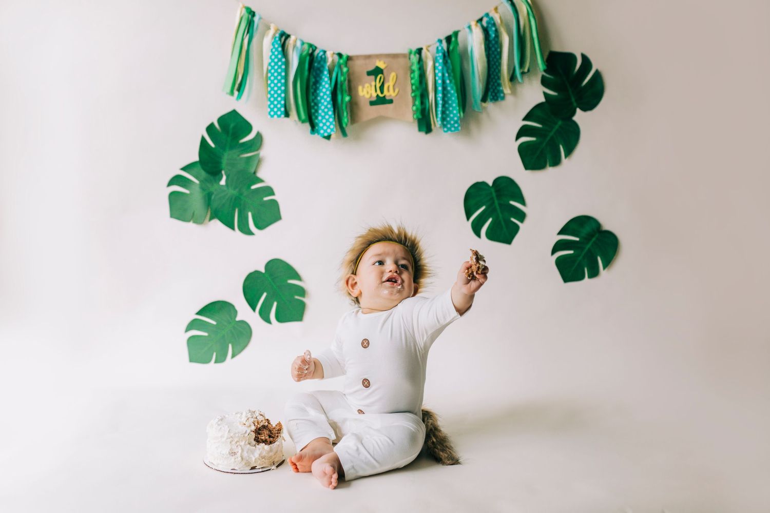 A collage of milestone photos showing a baby growing up against a white wall with green tropical leaf decorations.