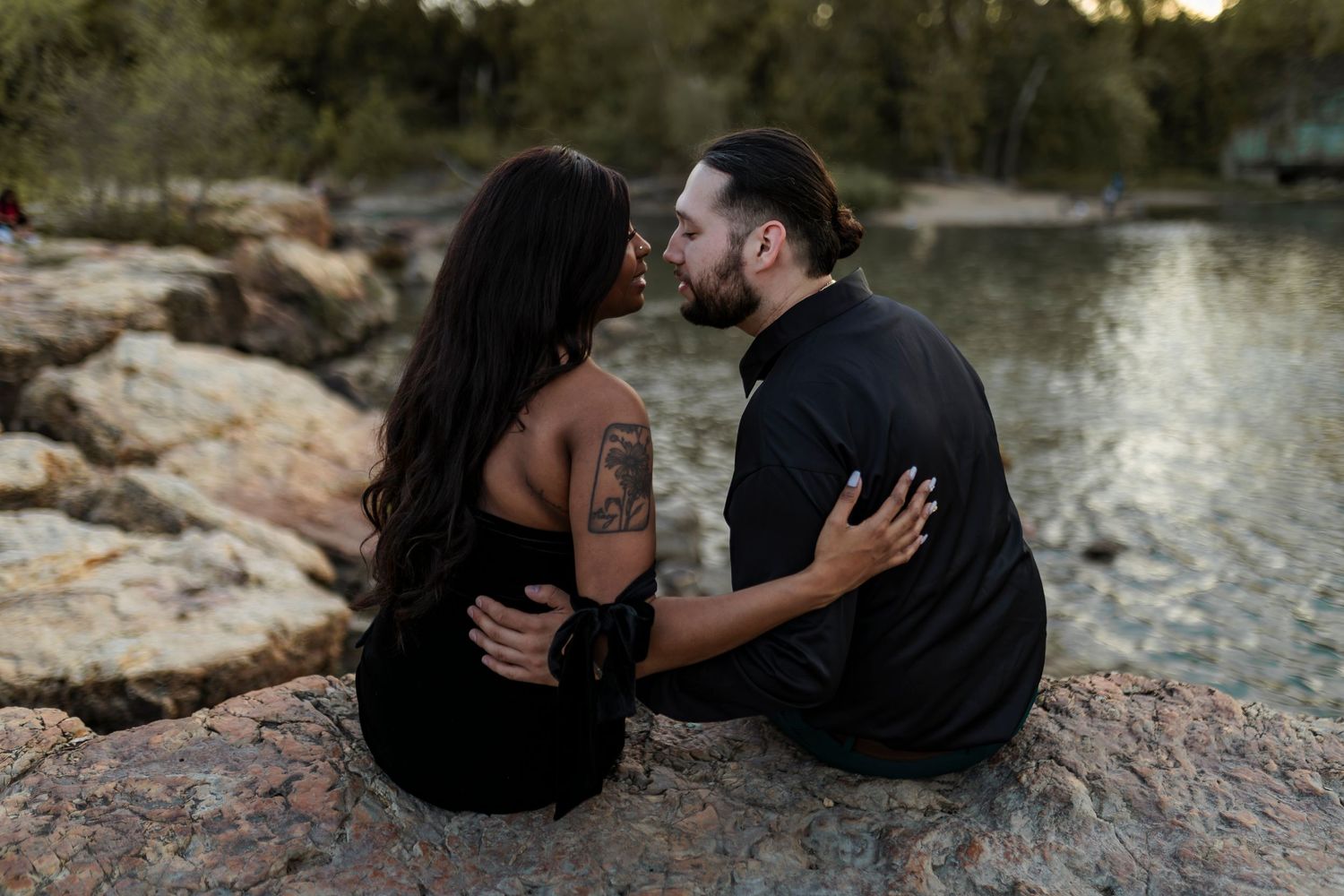 A couple shares intimate moments by a rocky riverbank during a romantic sunset photoshoot.