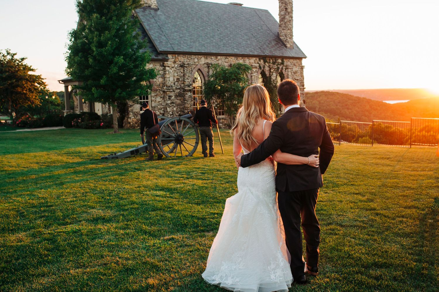 Newlyweds share romantic moment at sunset by stone chapel with cannon.