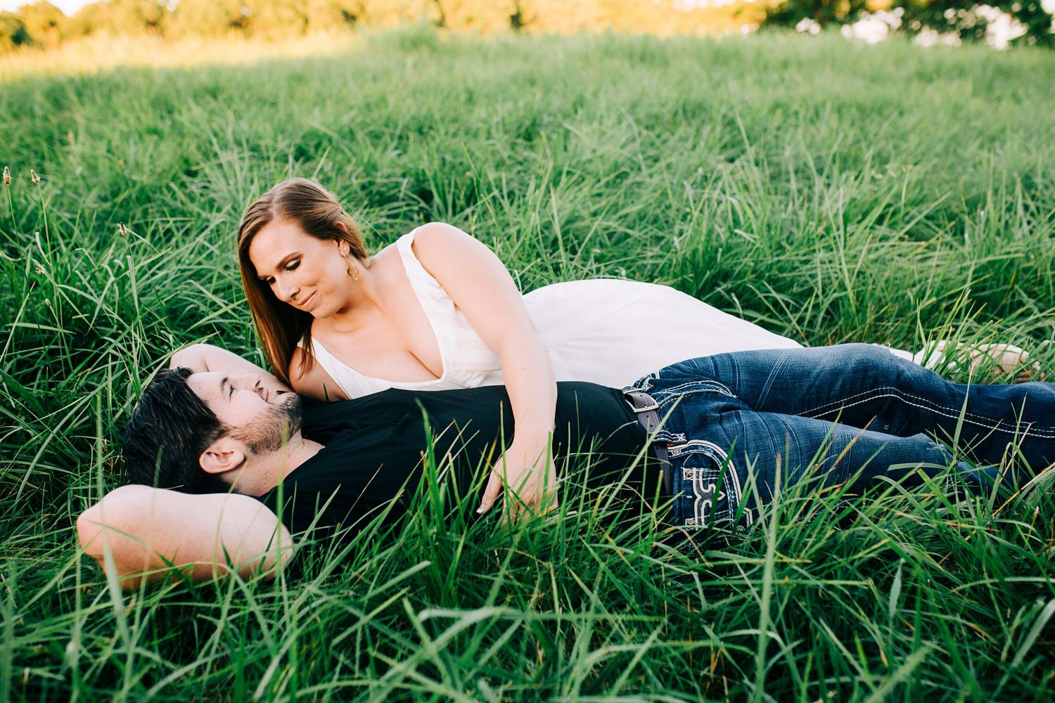 A couple lying together in tall grass during a warm summer day.