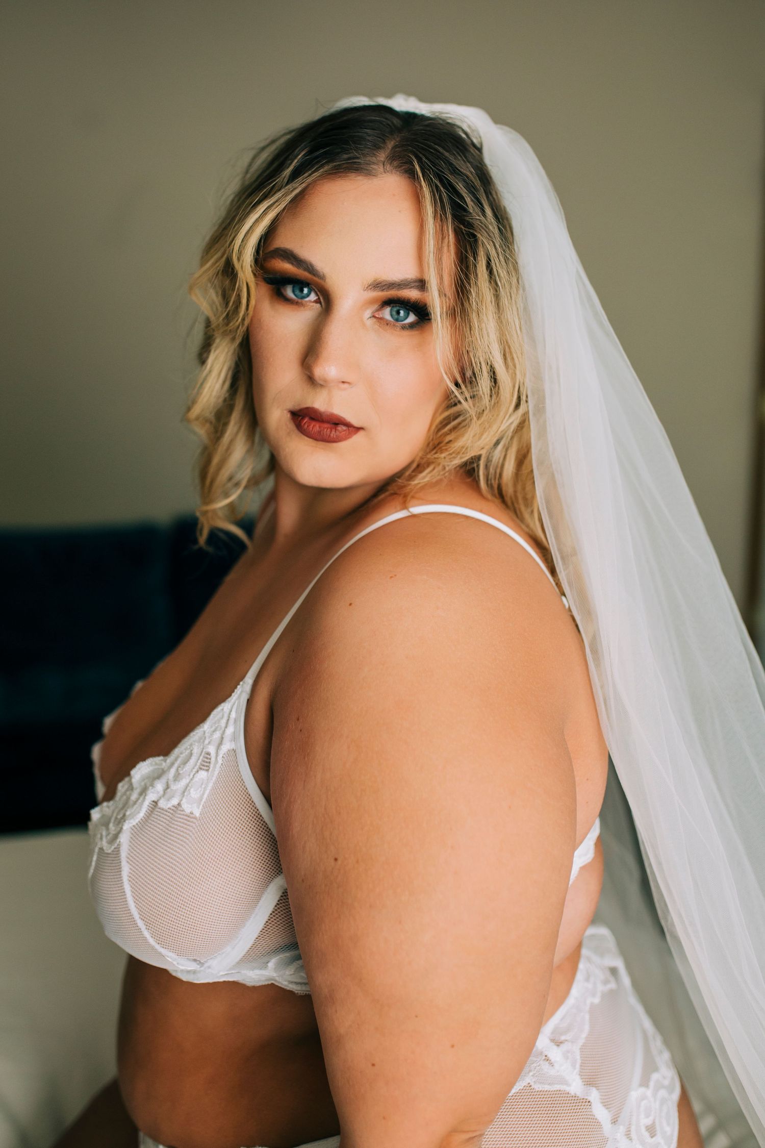 Bridal boudoir portrait series showing delicate white lace lingerie and veil in moody lighting.
