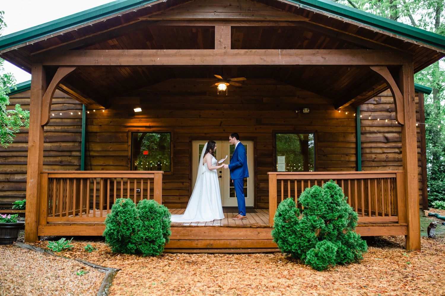 Elegant wedding ceremony under wooden pavilion with rustic cabin backdrop.