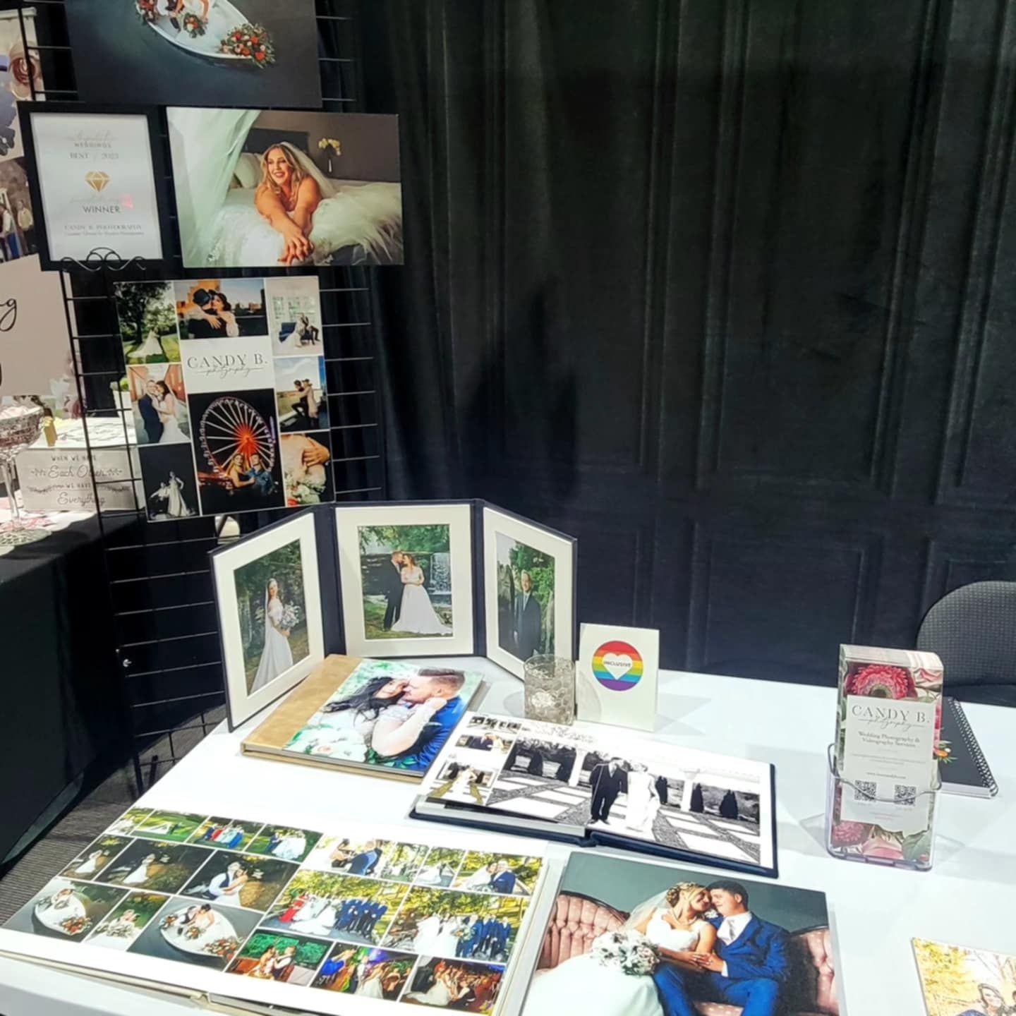 Collection of wedding and portrait photographs displayed on a dark surface with albums, prints and frames arranged together.