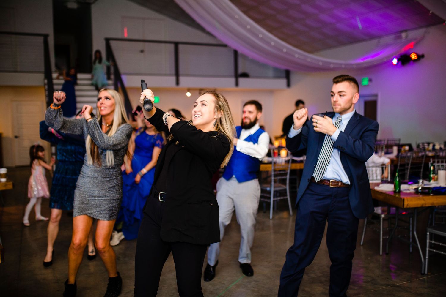 People dancing and having fun at a wedding reception with purple lighting and party atmosphere in an indoor venue.