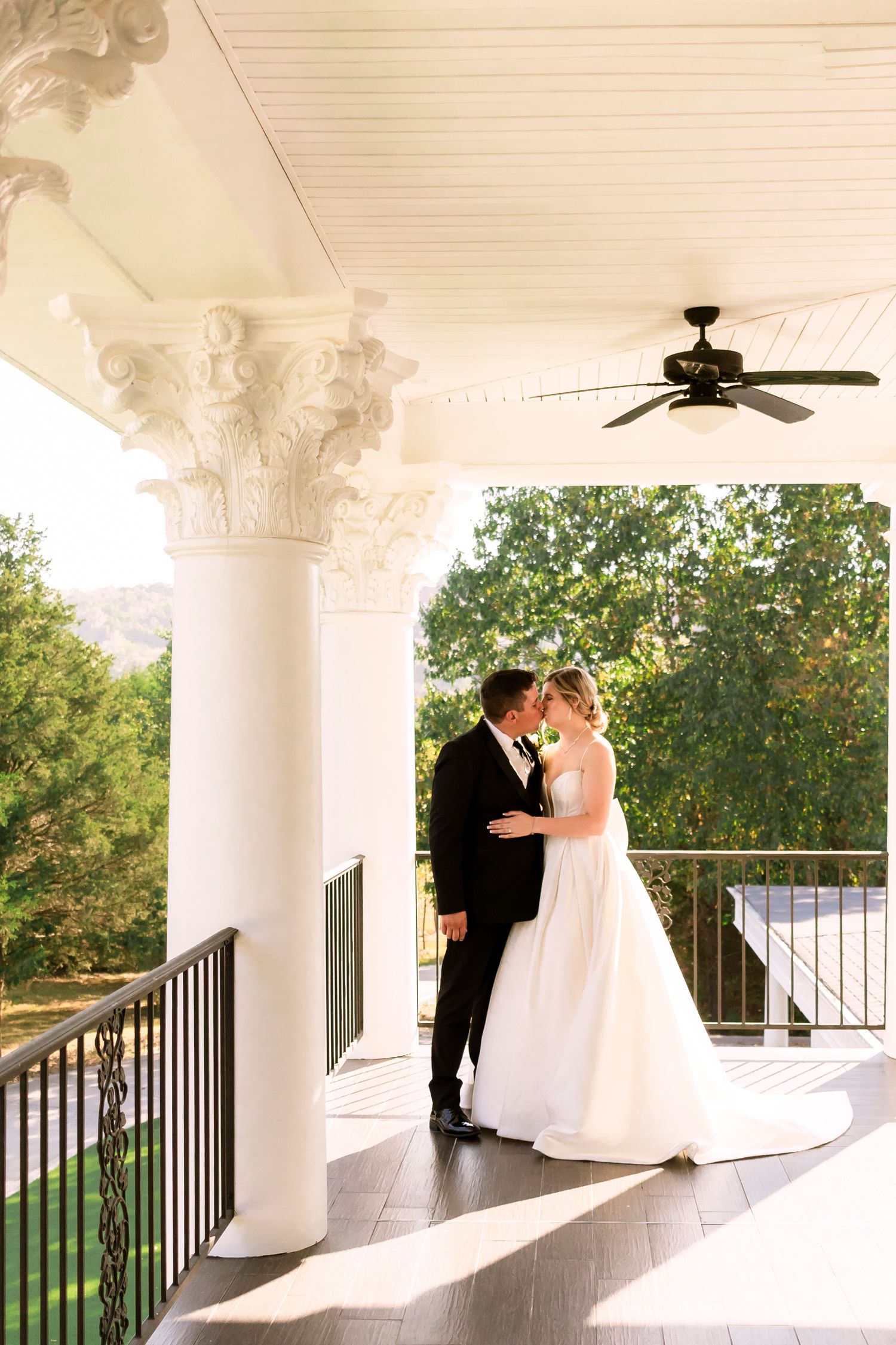 Wedding couple sharing intimate moment on elegant white columned porch.