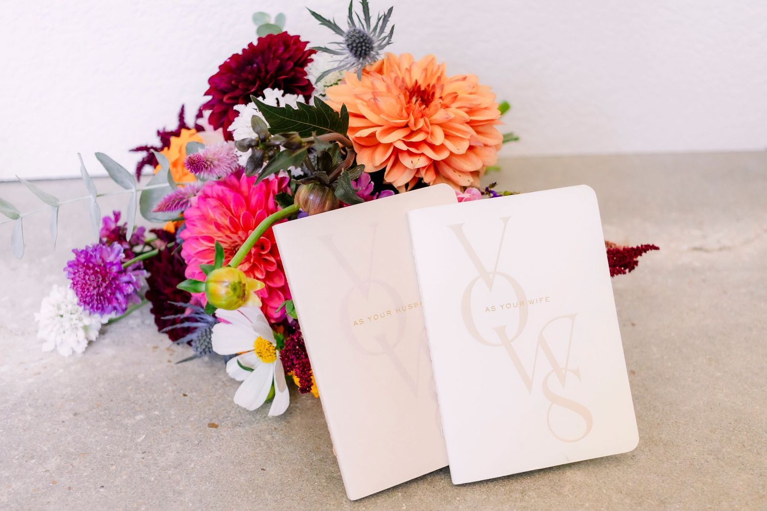 Colorful floral arrangement with pink and orange blooms next to white cards on neutral surface.