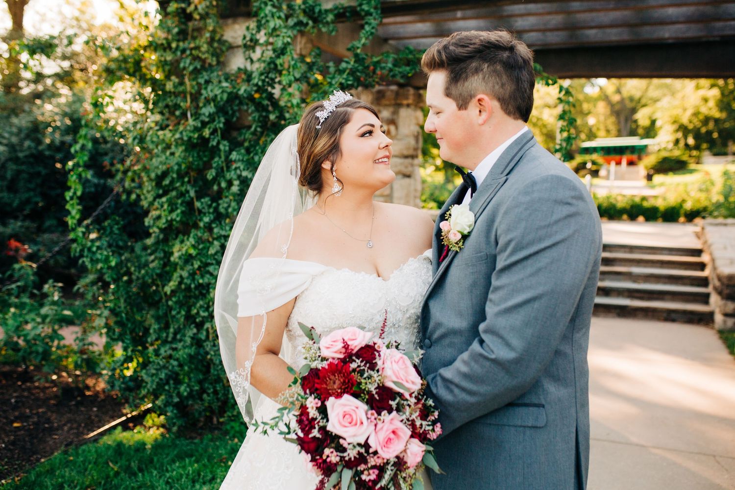 Newlyweds share tender moment in garden with pink rose bouquet at the Rose gardens in Kansas City Missouri.