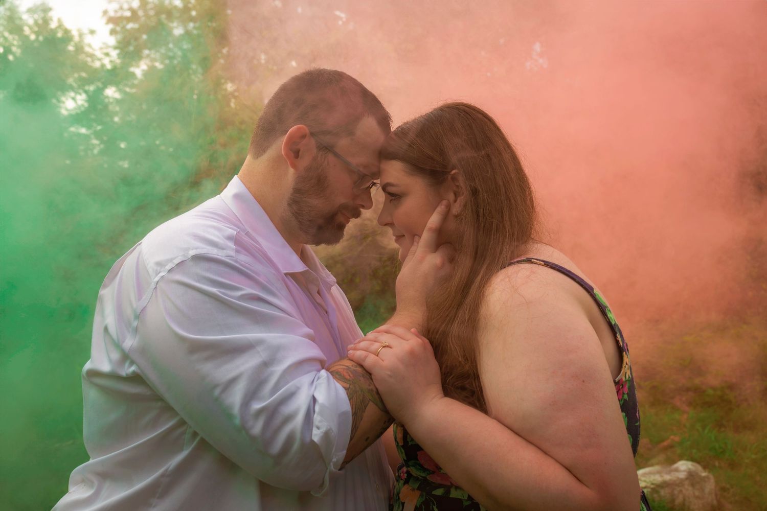 A couple shares a tender romantic moment in a dreamy forest setting with colorful smoke effects in the background.