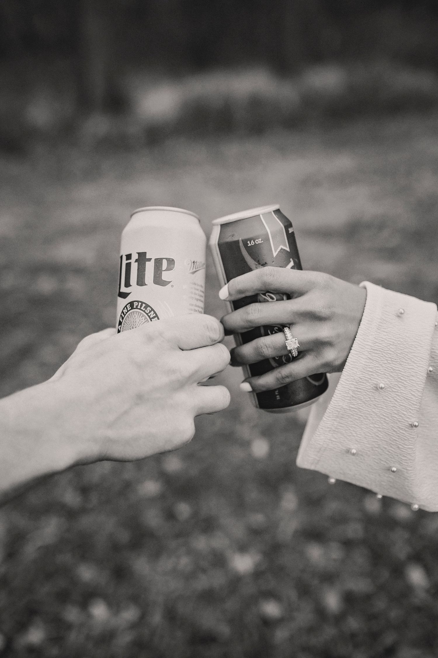 Black and white photo of two hands toasting with beer cans of Miller Lite outdoors.