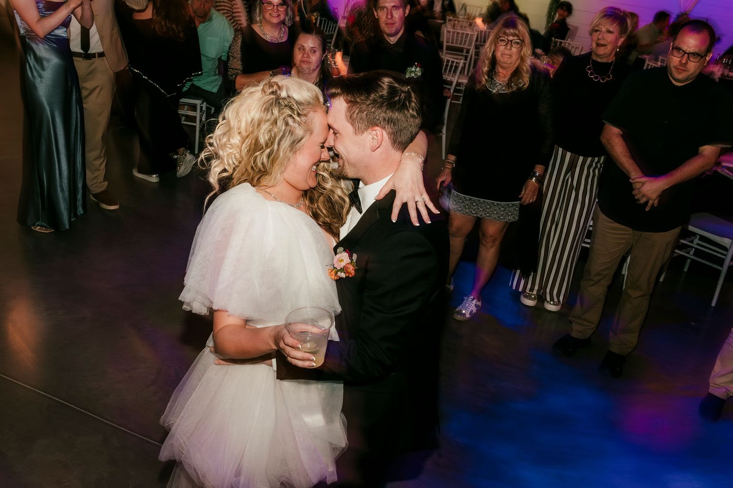 Two people share an intimate dance together on the dance floor while guests watch during a wedding celebration.