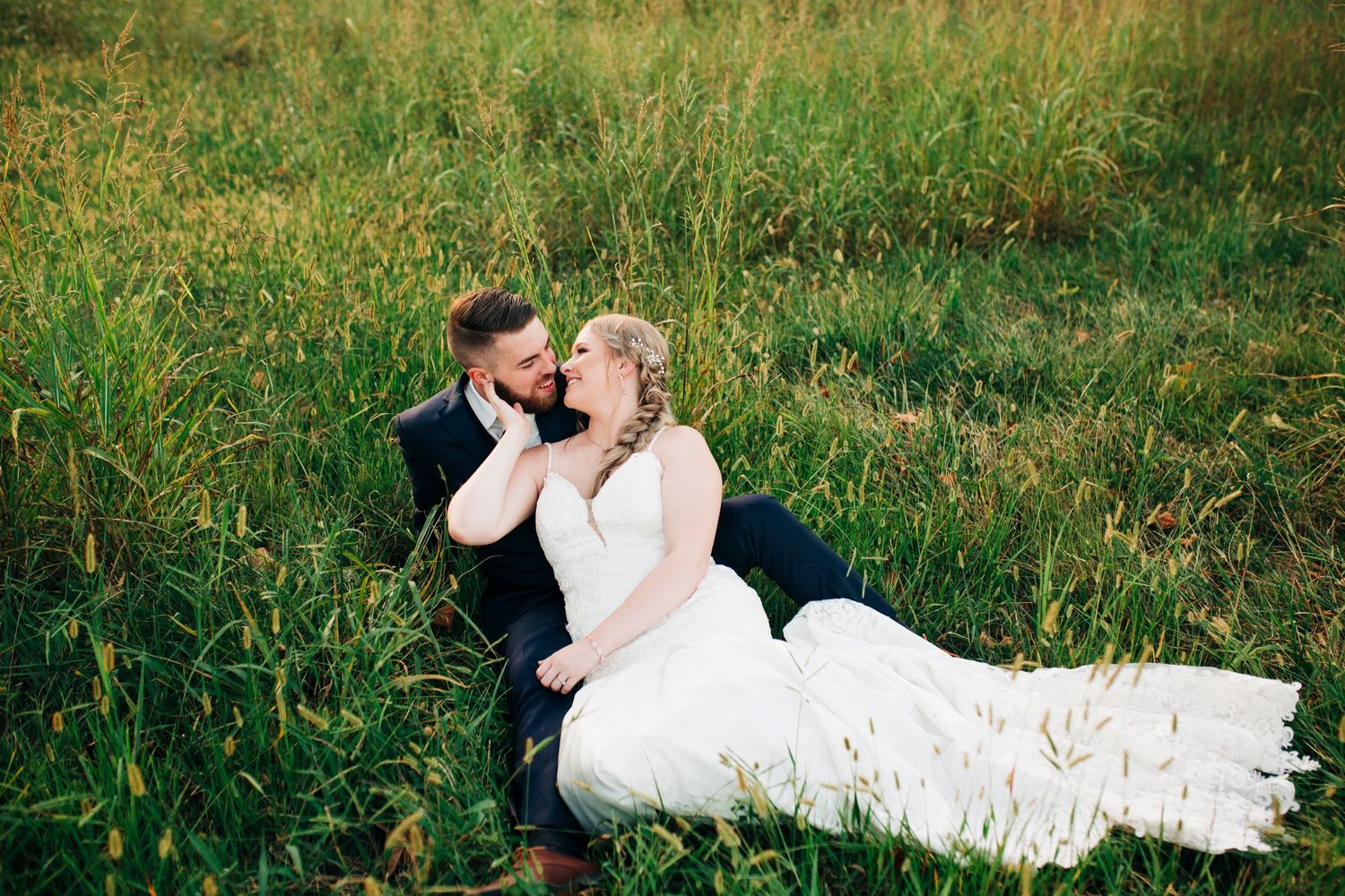 Couple shares tender moment while sitting in green summer field.