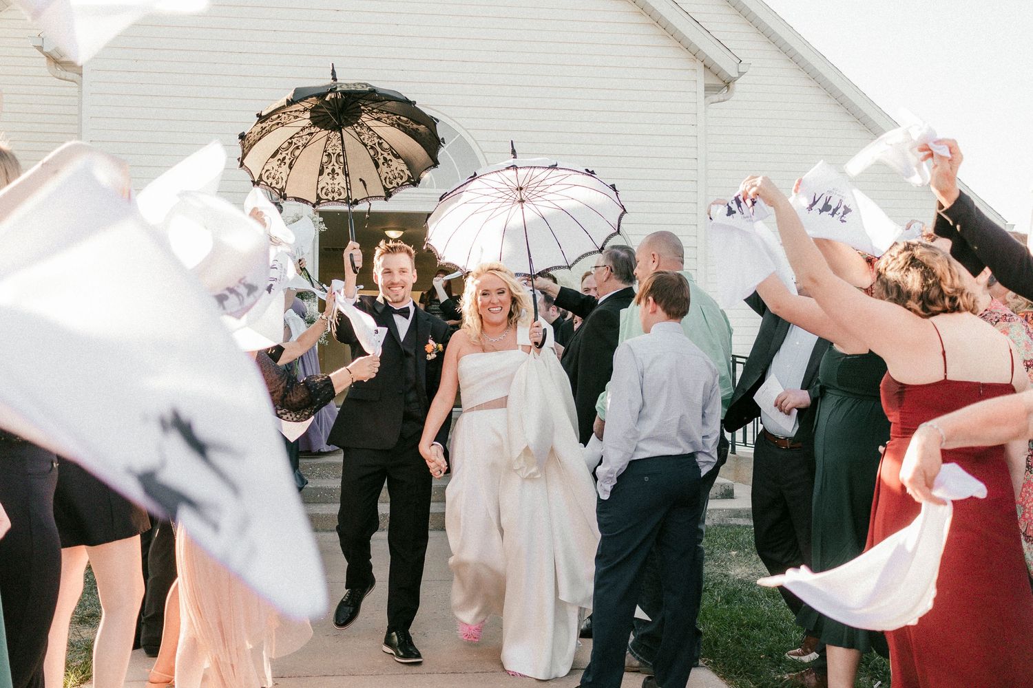 Wedding guests celebrate with white parasols outside a white building during an elegant outdoor reception.
