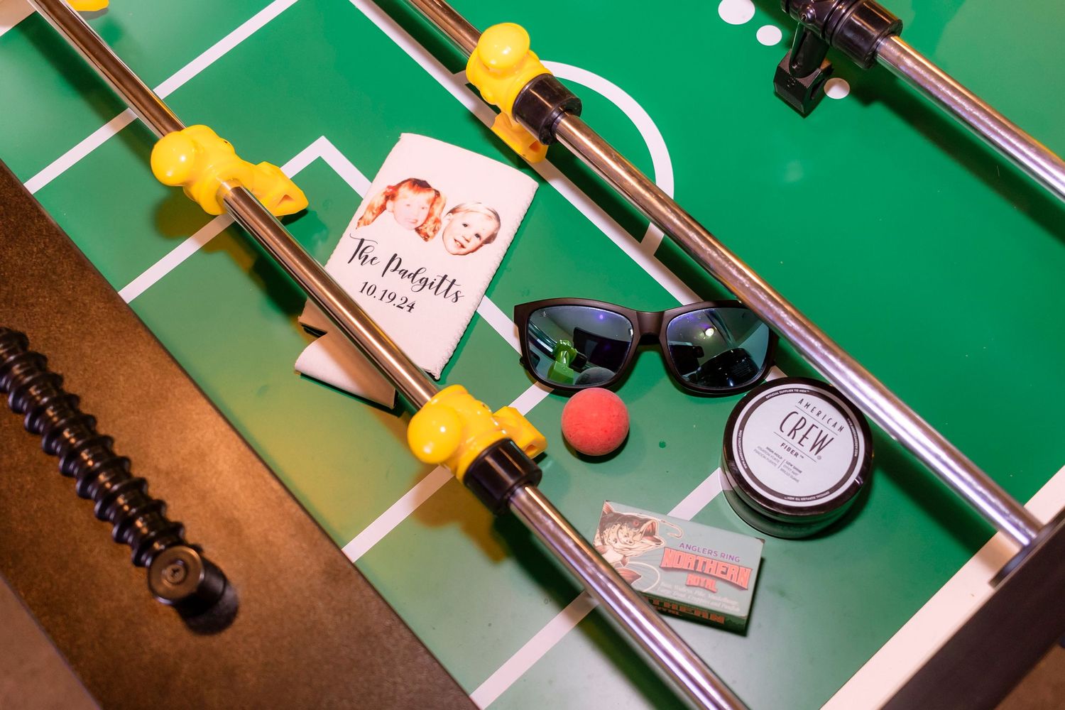 A foosball table with sunglasses, sticky notes and accessories shown from above on its green playing surface.