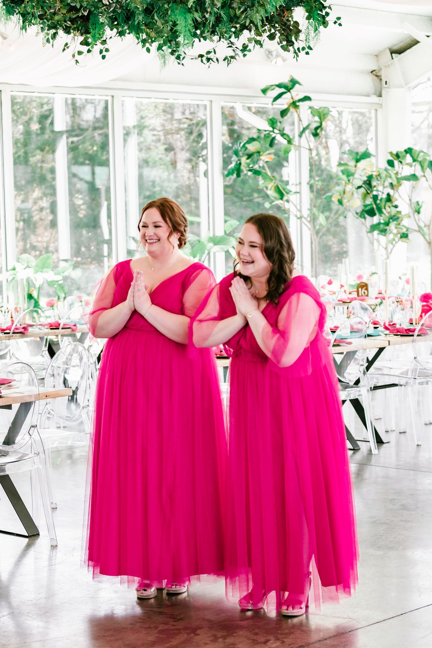 Two bridesmaids share a joyful moment in a bright sunlit reception space at Green House Two Rivers in Highlandville Missouri .