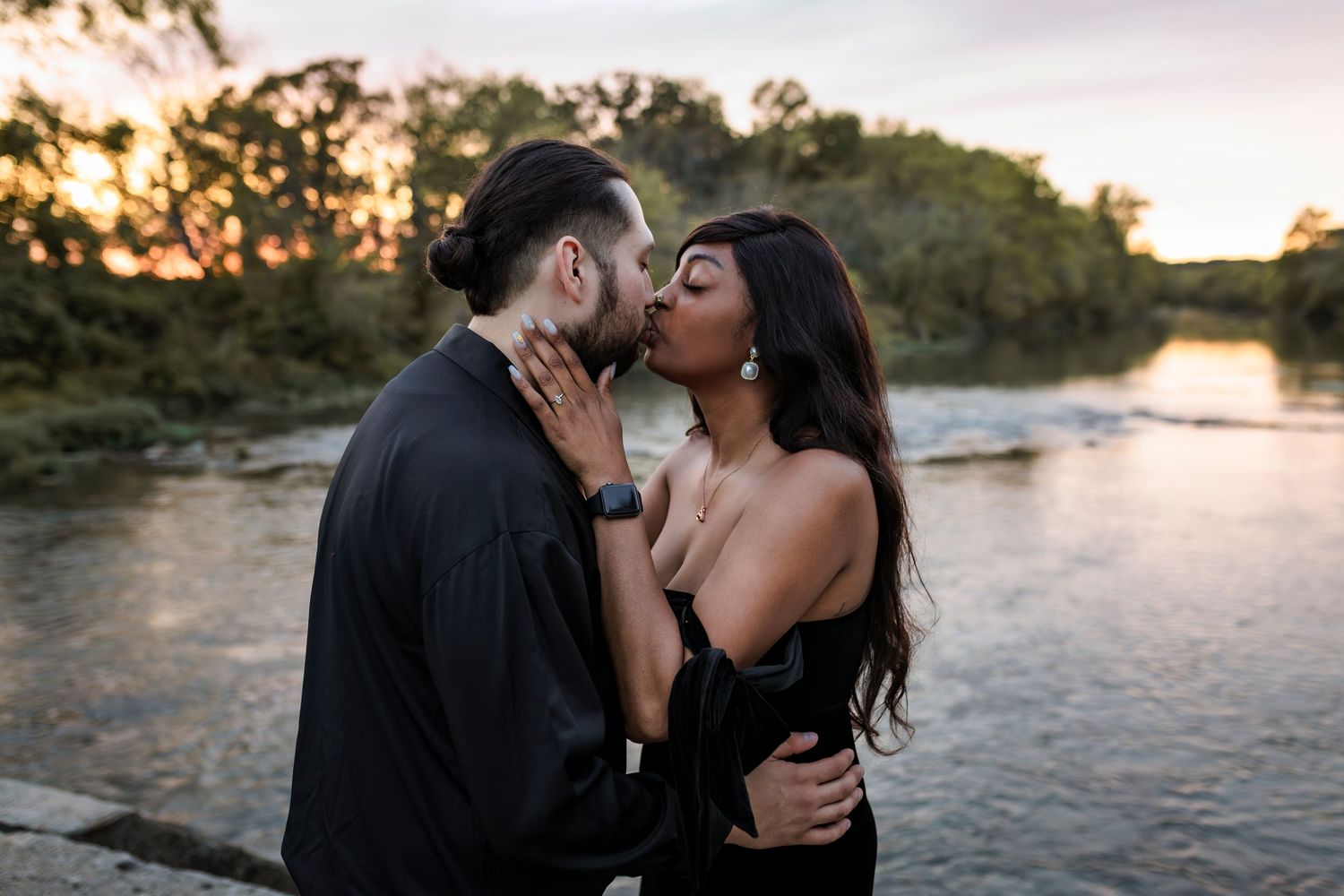 Romantic couple embraces at sunset by a river with golden light illuminating their intimate moment.