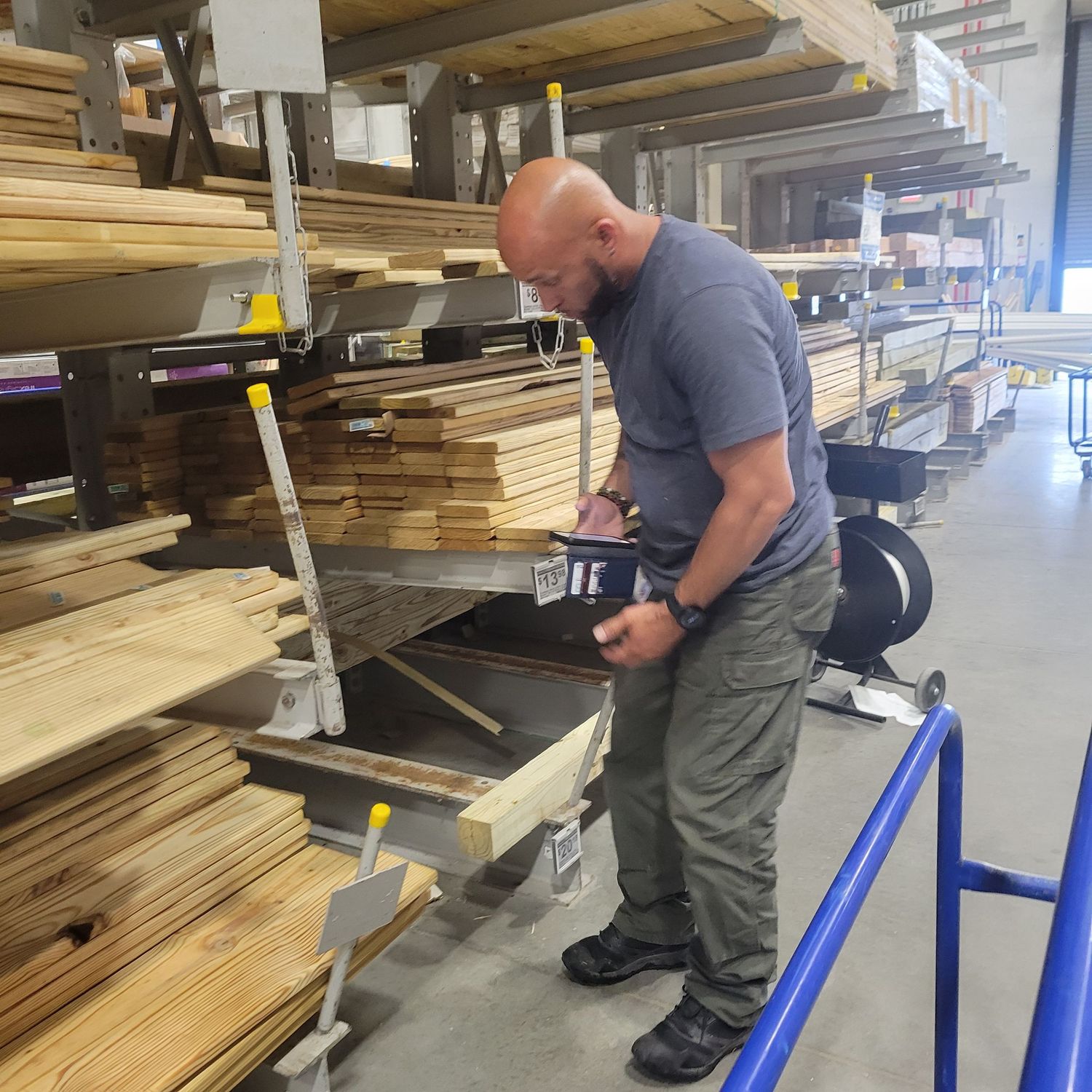 Worker selecting lumber from organized storage racks in a warehouse supply store.
