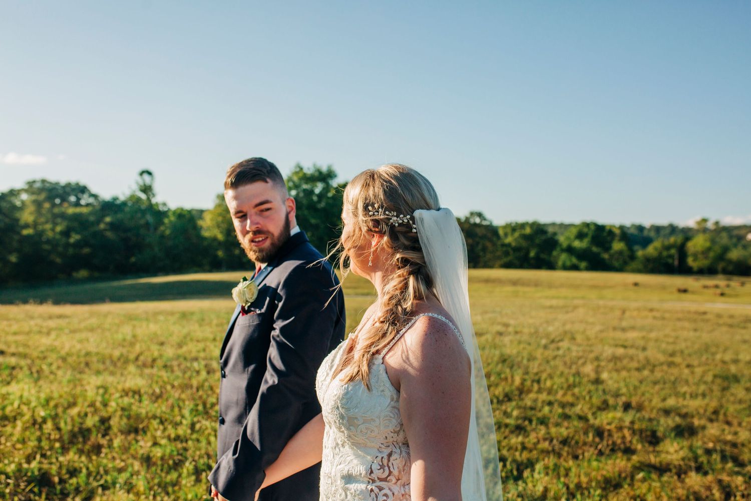 Wedding couple shares candid moment in sunlit field during golden hour.