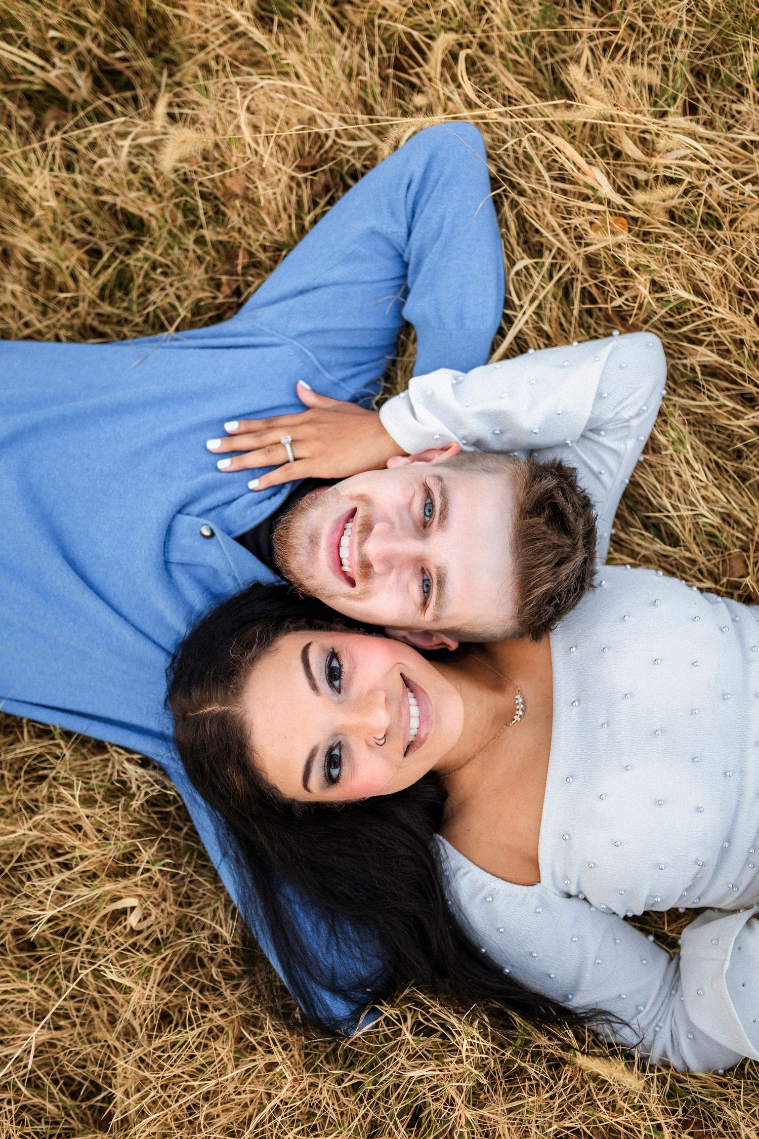 Couple lying on golden hay in casual attire sharing loving moment together.