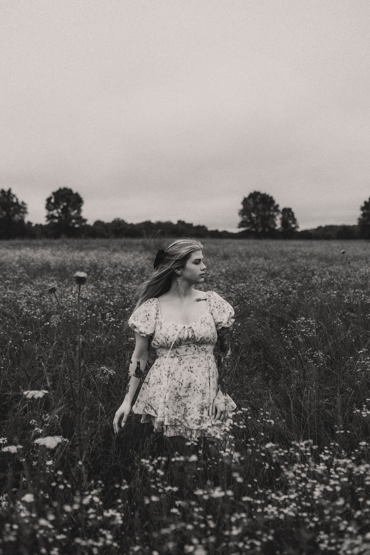 A person in a floral dress walks through a wildflower meadow on an overcast day in black and white.