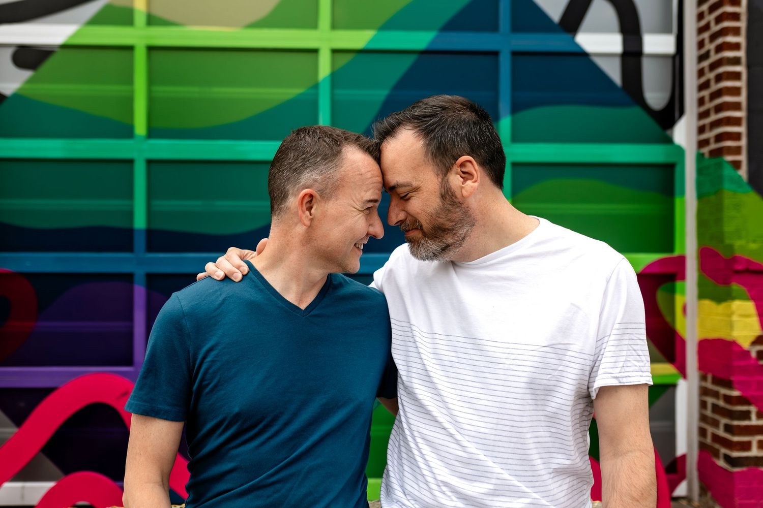 Close intimate moment between two people against colorful rainbow mural wall in The Grove in St. Louis MO.