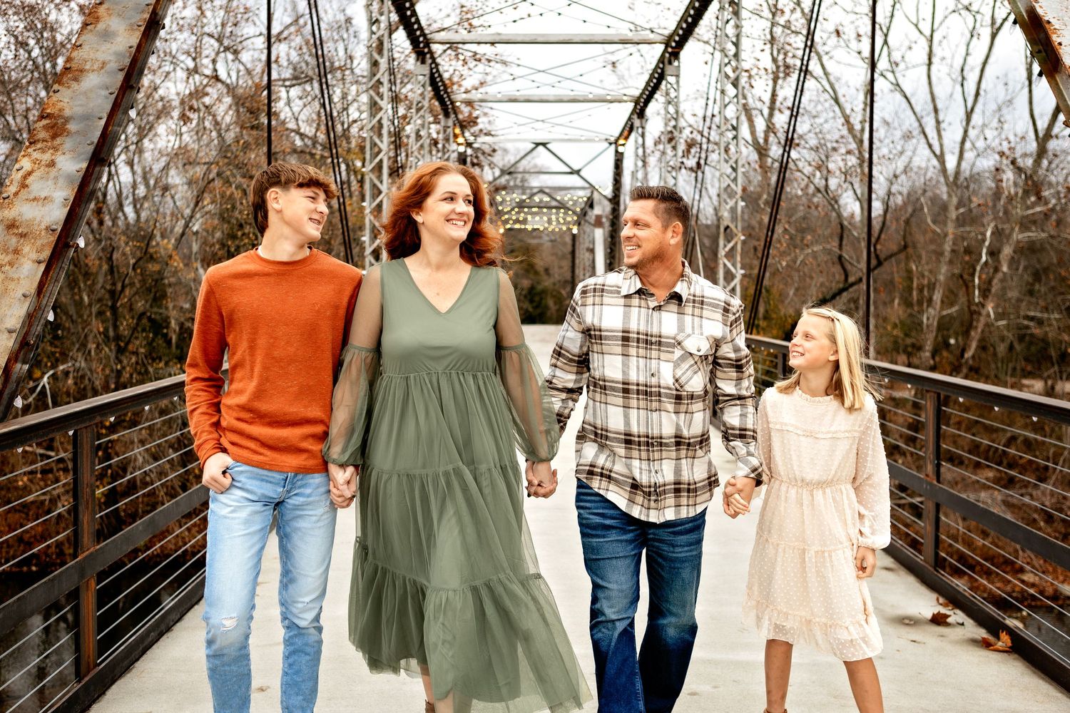 Four people walking together on a rustic metal bridge during autumn with trees in the background.