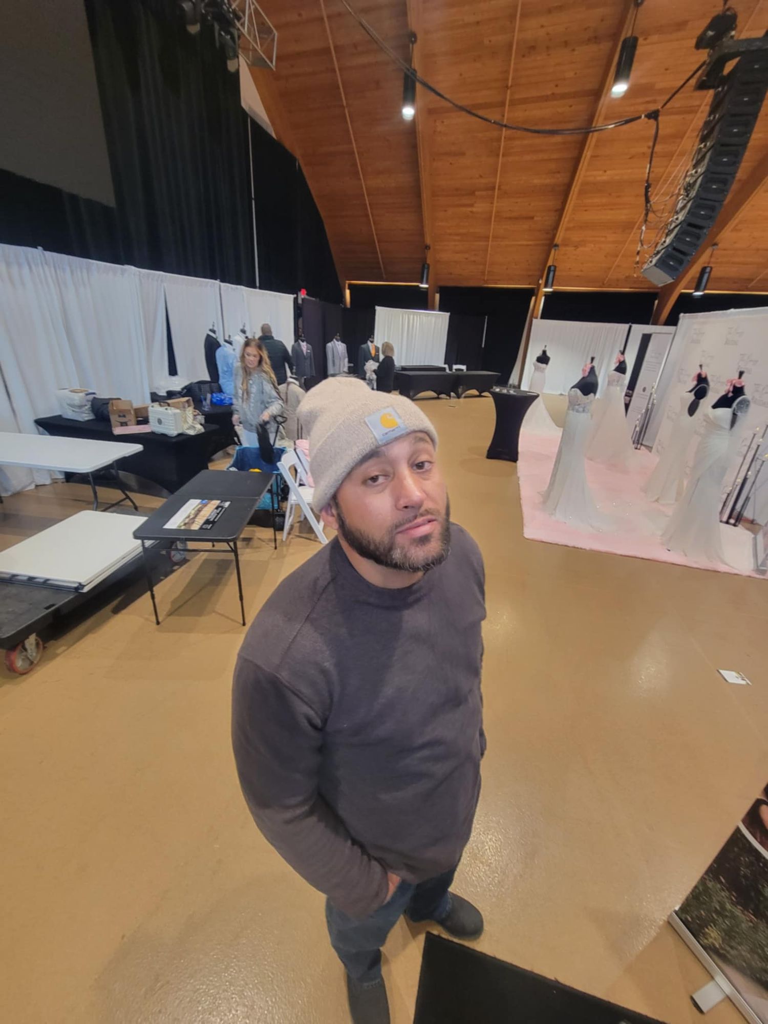 Person wearing a grey beanie and sweatshirt poses in what appears to be a photography or event setup space.