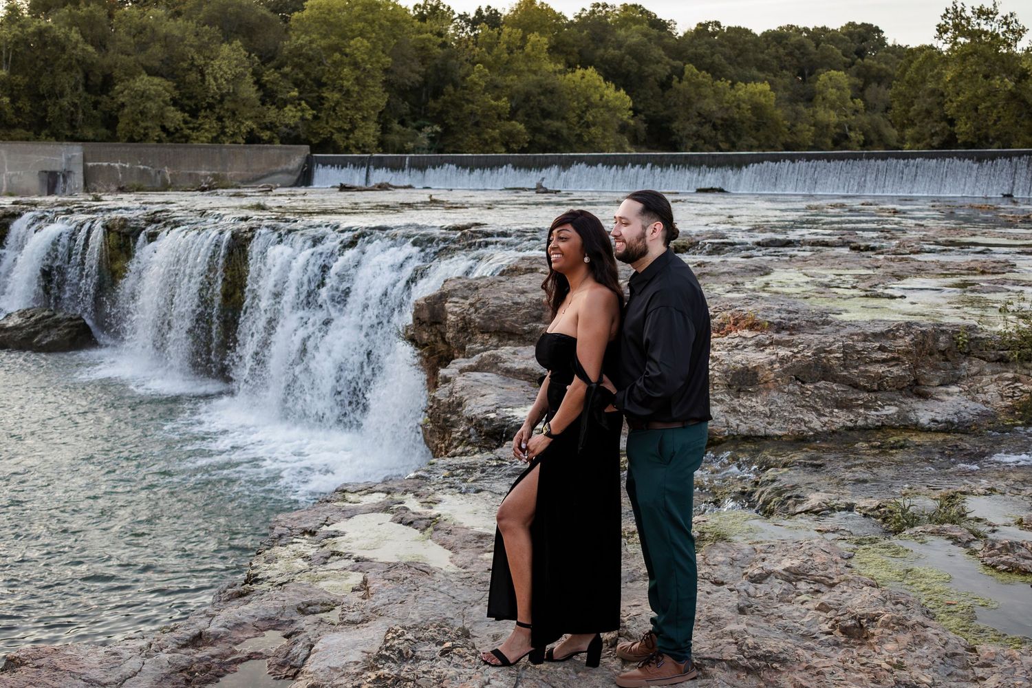A couple enjoys a romantic moment beside cascading waterfalls in a scenic natural setting.