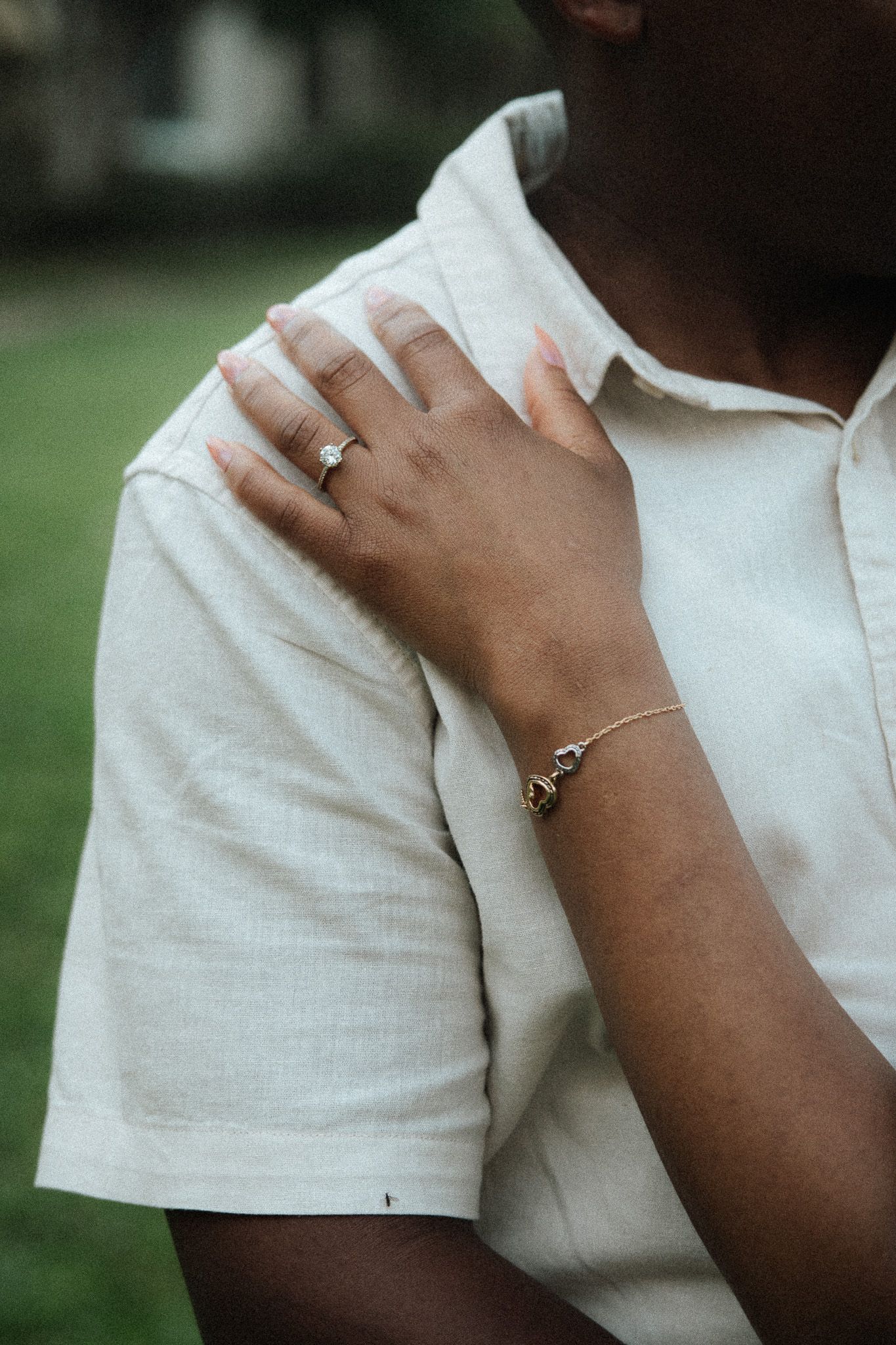 Close-up of a woman's hand on a man's shoulder showing an engagement ring and gold bracelet.