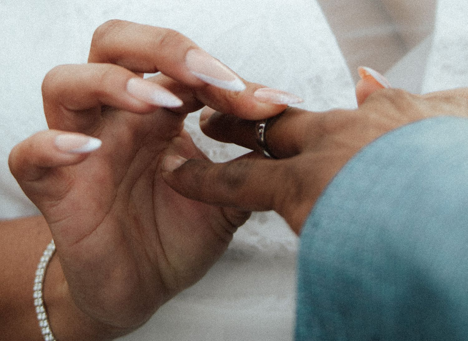 Close-up of hands exchanging a wedding ring during a ceremony, with manicured nails and a pearl bracelet visible.