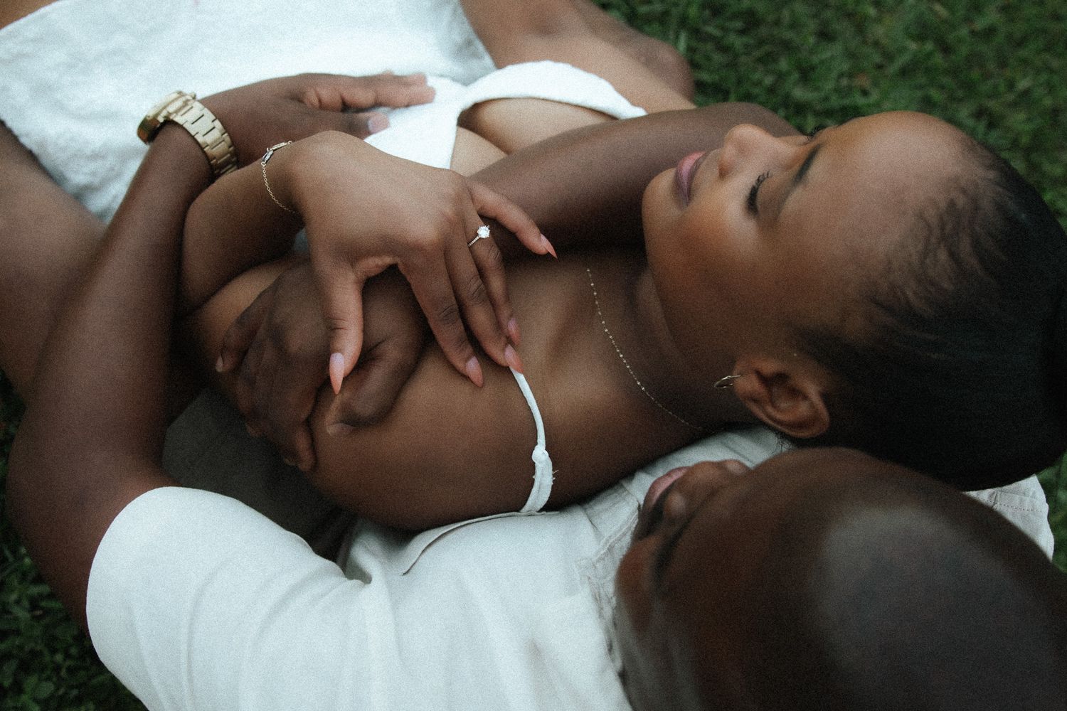 A couple lying on grass, hands intertwined, in an intimate and tender close-up moment.
