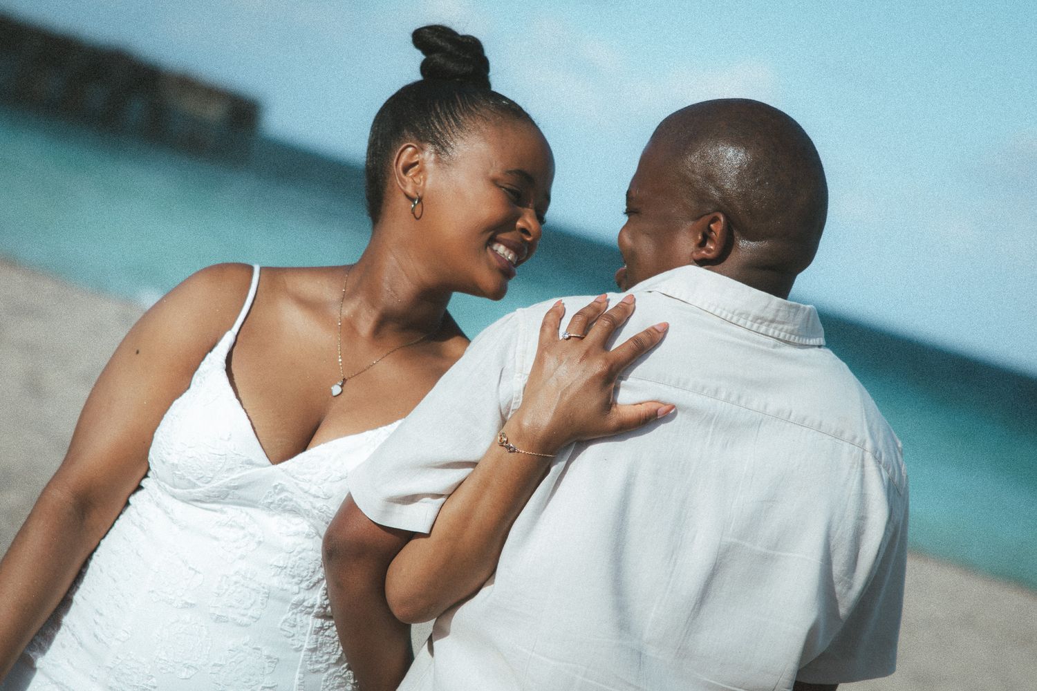 A happy couple laughing and sharing a joyful moment together on a sunny beach with blue ocean water behind them.