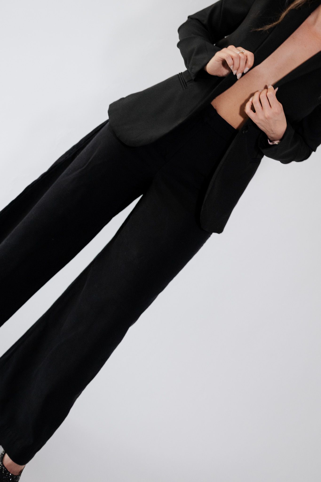 Close-up of woman in black wide-leg trousers and blazer suit against white background.