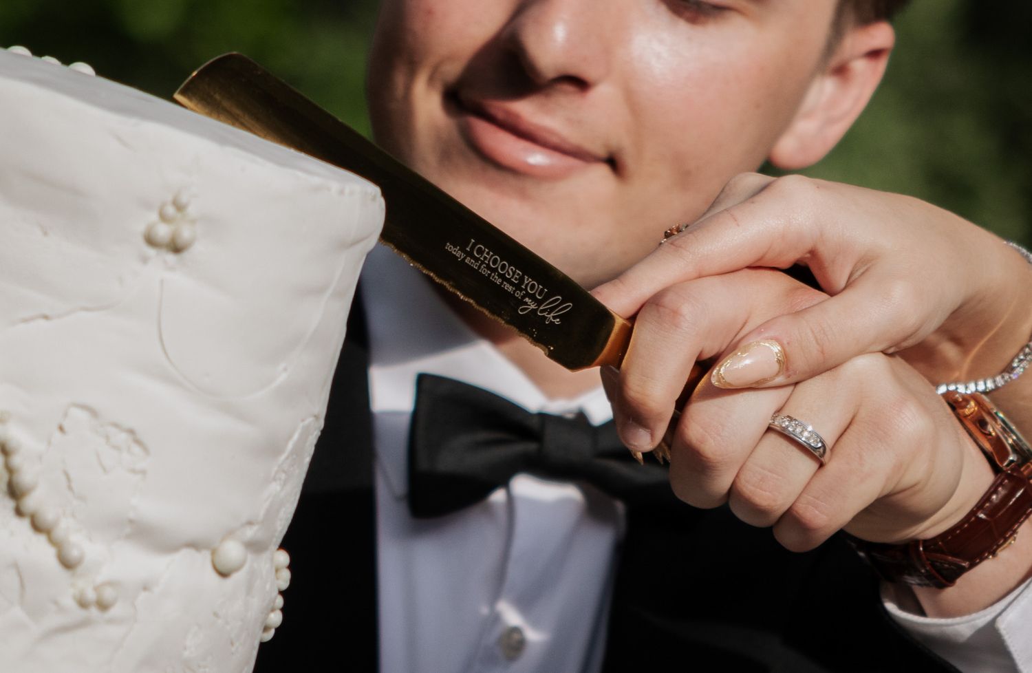 Close-up of smiling groom and bride cutting white wedding cake with a gold engraved cake knife together.