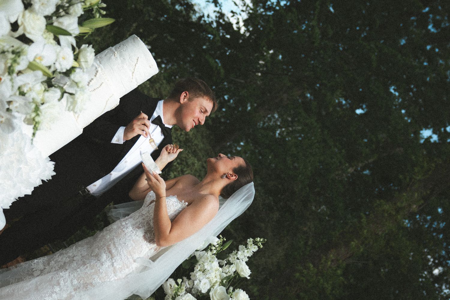 Bride and groom sharing an intimate moment while cutting their white wedding cake in an outdoor garden setting.