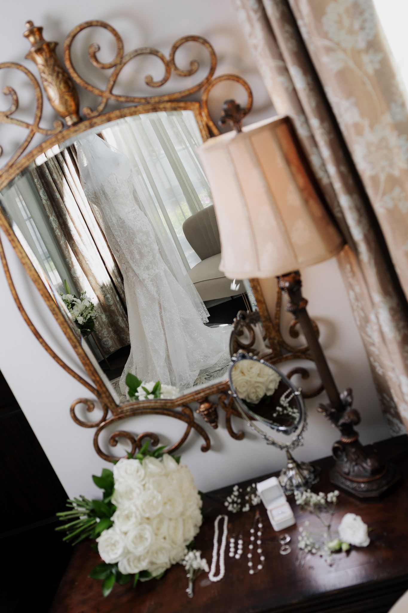 Ornate gold mirror reflecting a lace wedding dress with white roses and bridal accessories.