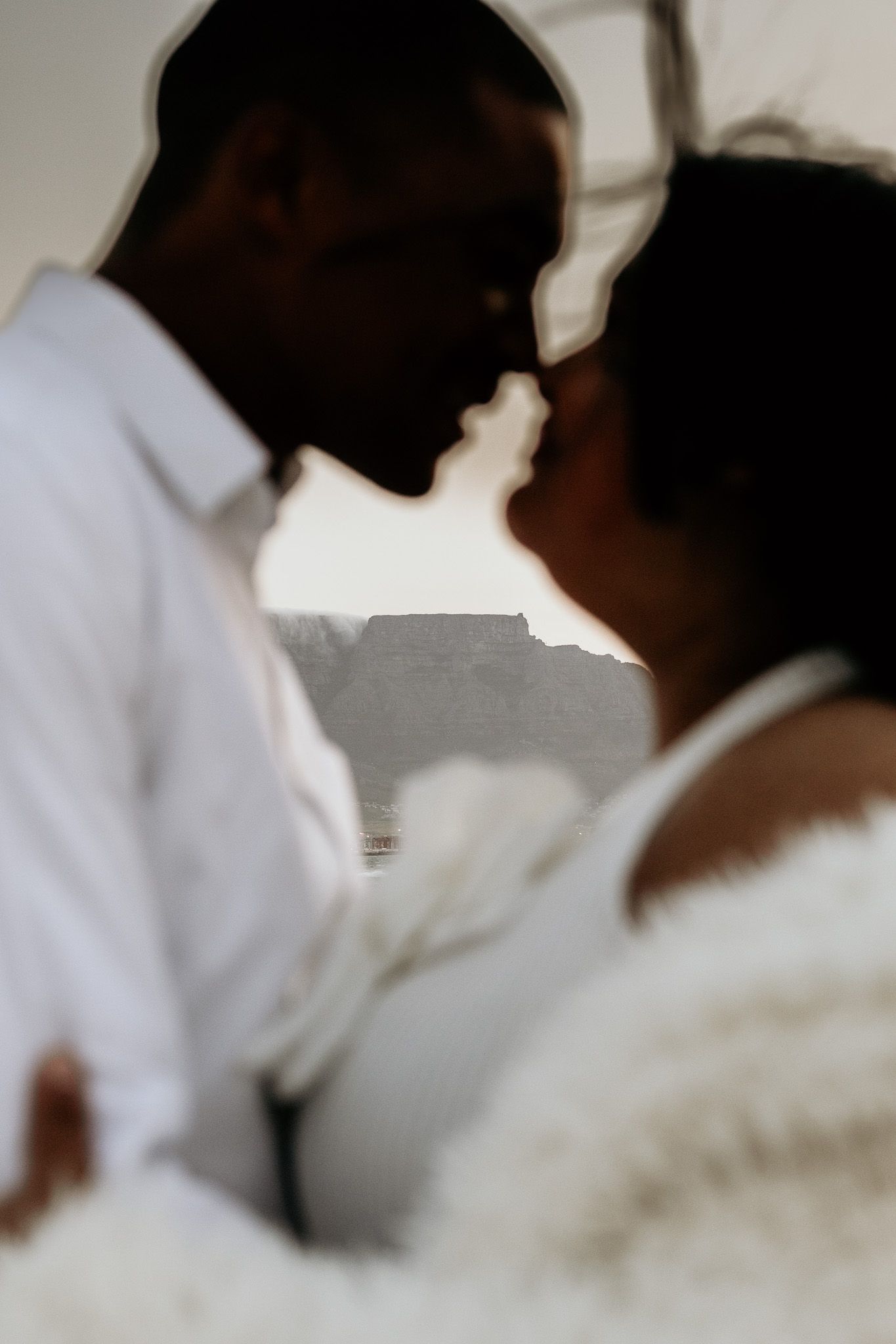 Intimate close-up of couple nearly kissing with Table Mountain softly blurred in background.