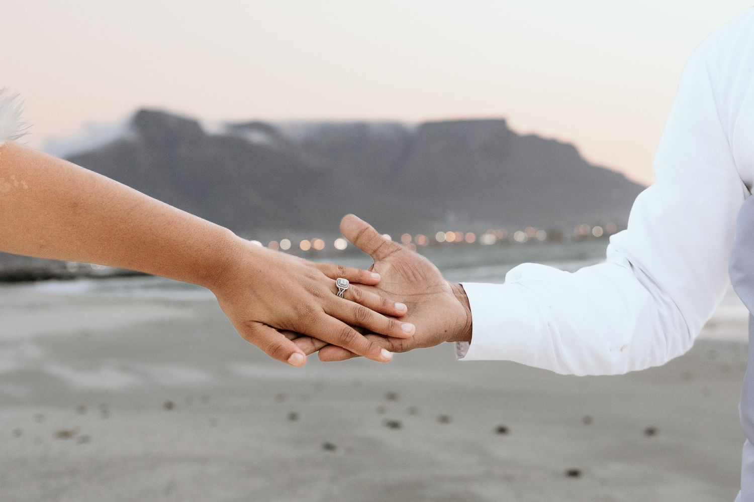 Close-up of couple holding hands showing engagement ring with Table Mountain in background.