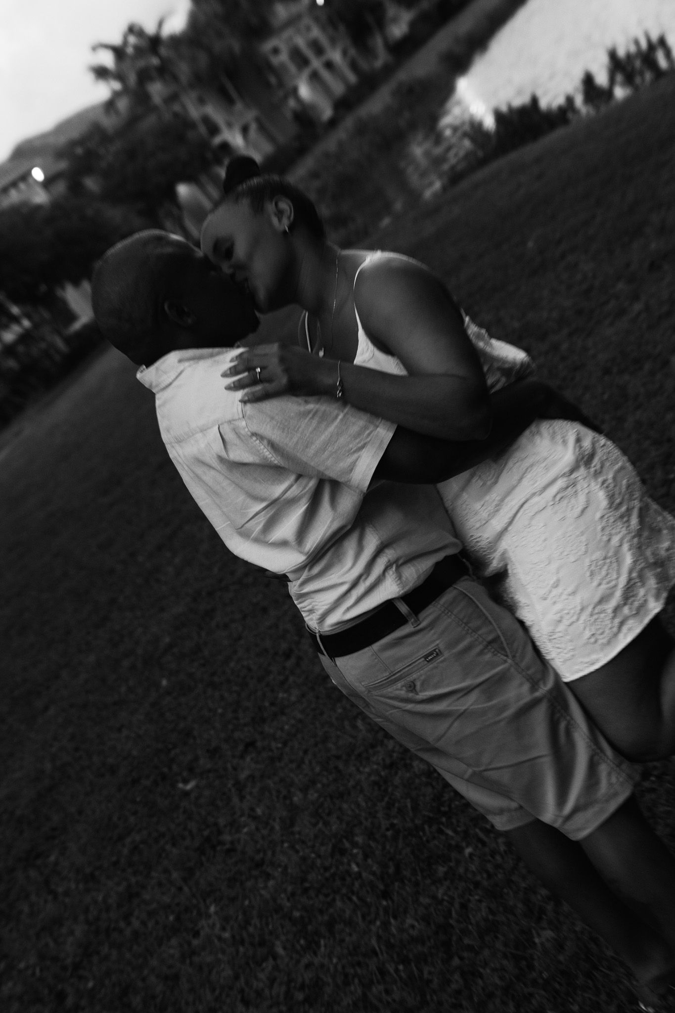 A romantic black and white photo of a couple sharing a passionate embrace and kiss at dusk outdoors.