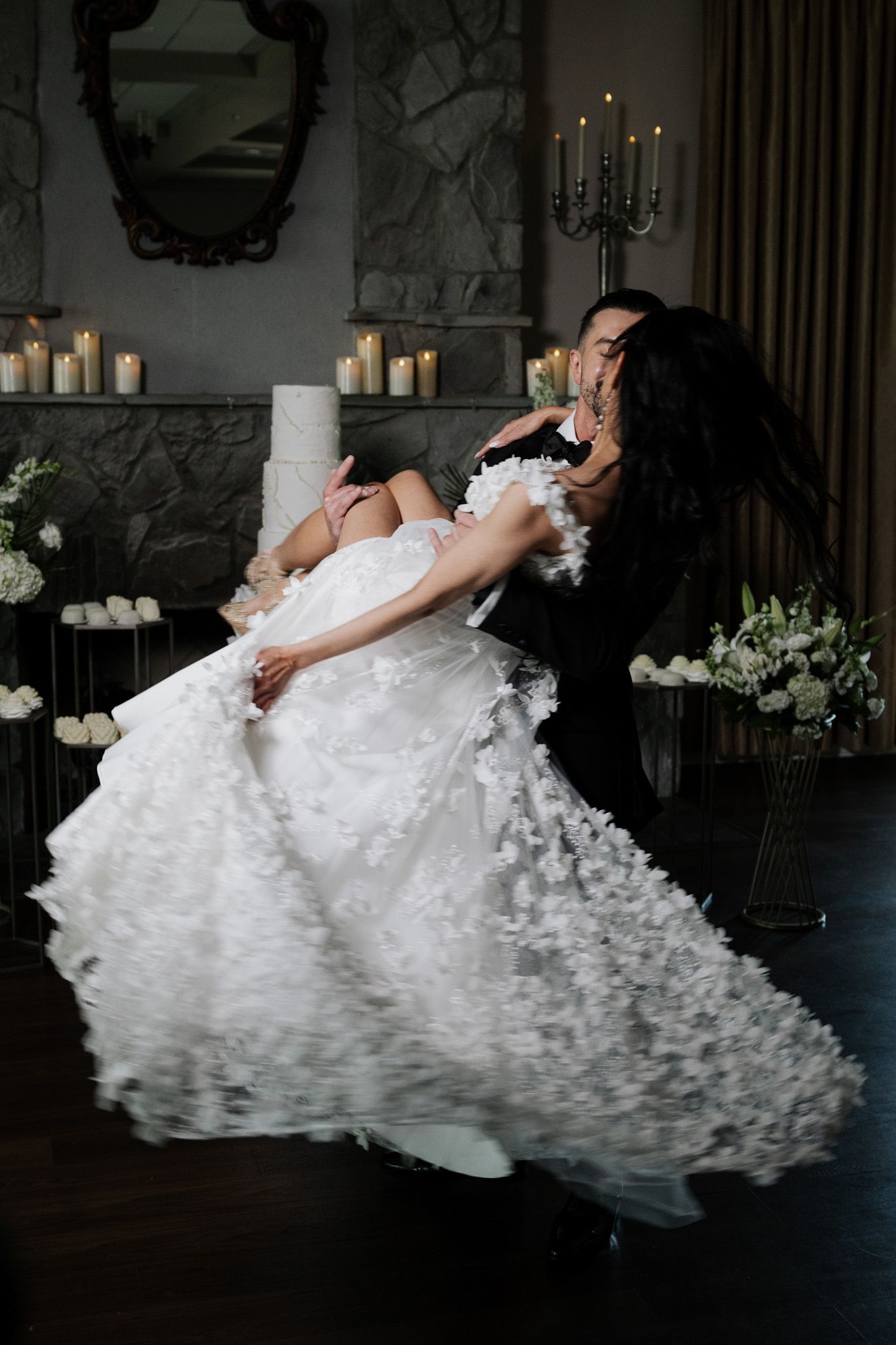 Groom dips bride in floral wedding gown during romantic first dance by candlelight.