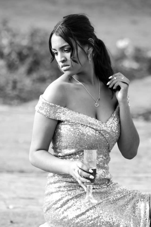 Elegant woman in sequin off-shoulder gown holding a champagne glass in black and white.